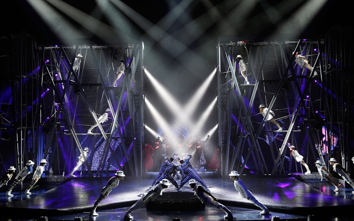 Performers in white suits and hats lean forward on stage during Michael Jackson ONE show.