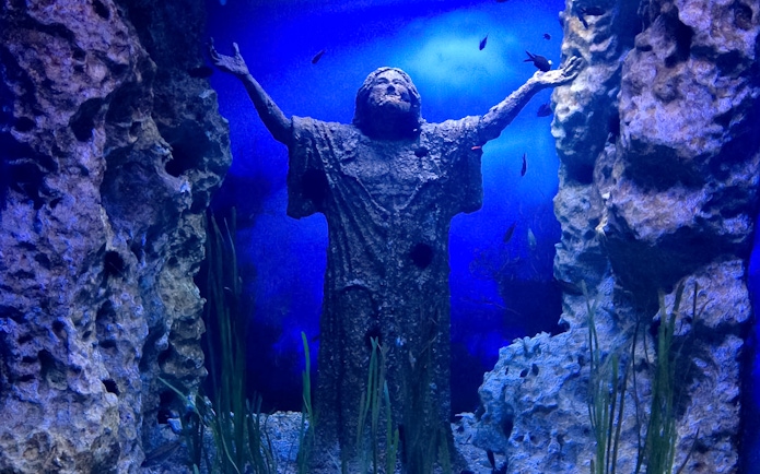 Statue with outstretched arms underwater at Malta National Aquarium.