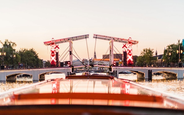 Amsterdam canal cruise view of illuminated Magere Brug at sunset.