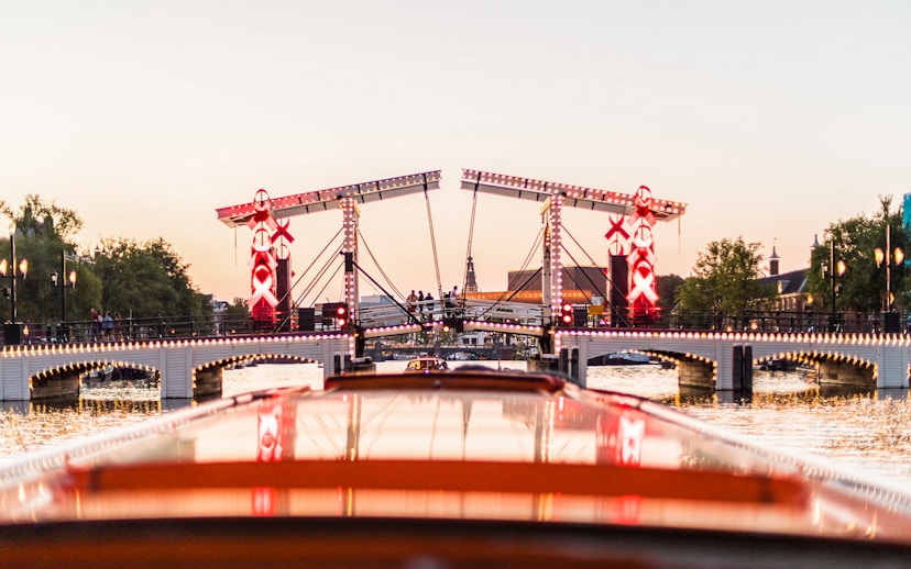 Amsterdam canal cruise view of illuminated Magere Brug at sunset.