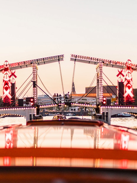 Amsterdam canal cruise view of illuminated Magere Brug at sunset.