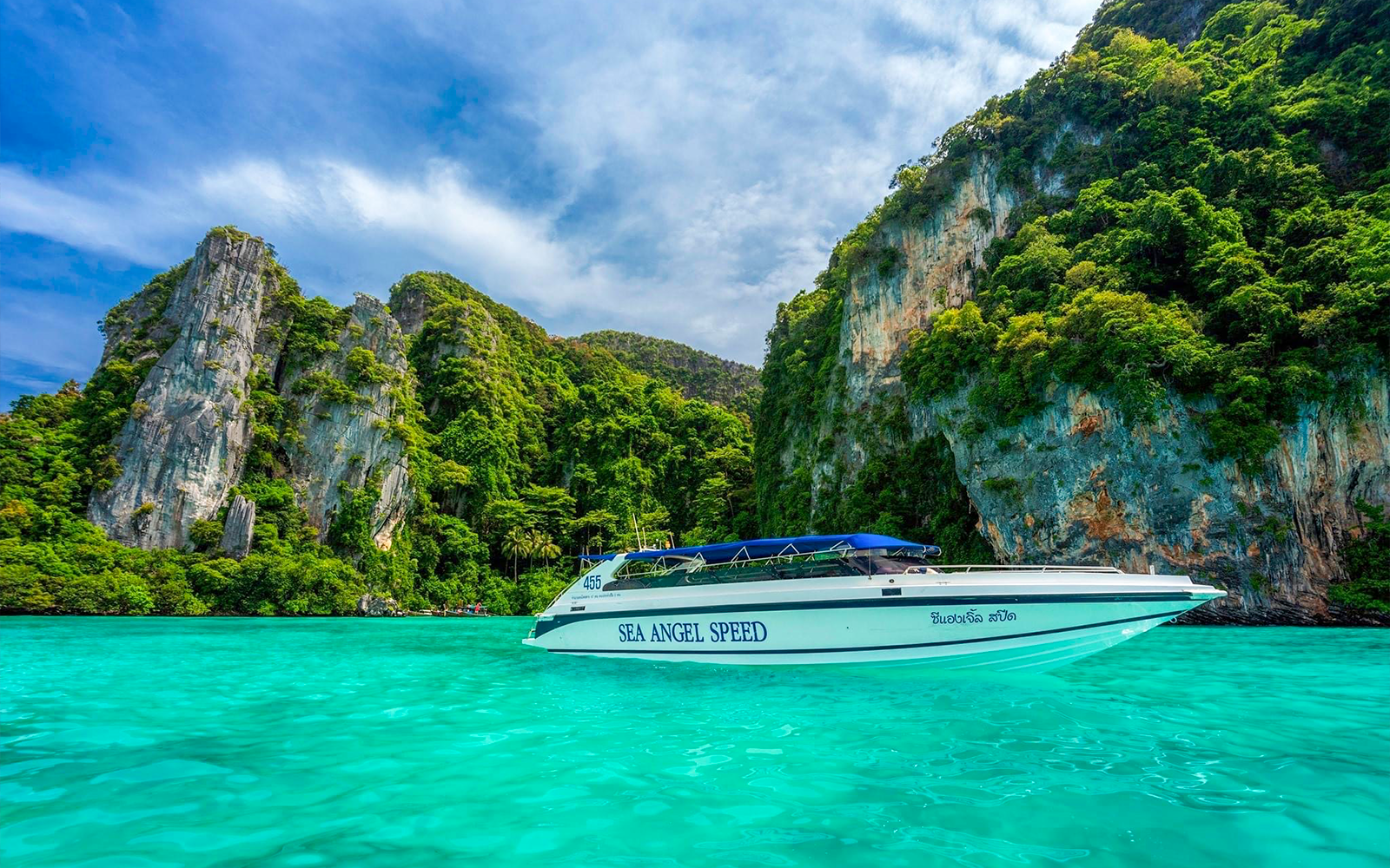 Speedboat navigating turquoise waters near rocky islands in Phi Phi, Thailand.