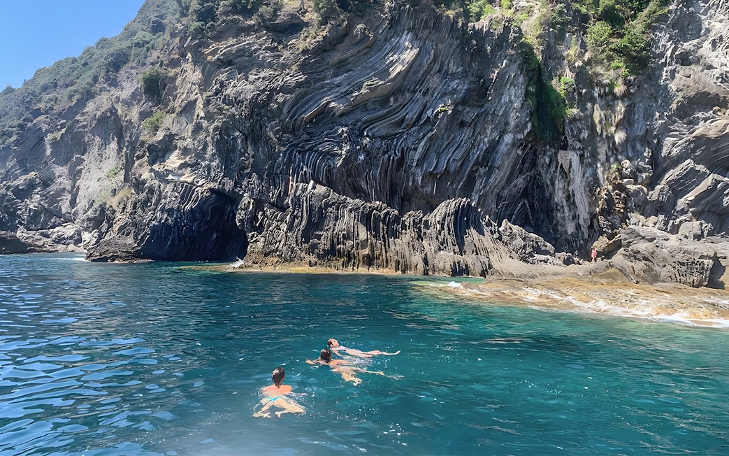 Swimmers near rocky cliffs on a guided boat tour of Cinque Terre from La Spezia.