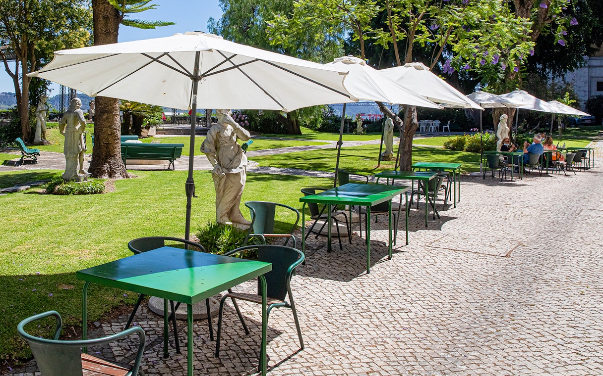 Outdoor café seating with statues in the garden of the National Museum of Ancient Art.