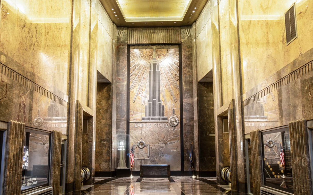 Empire State Building Art Deco lobby with golden ceiling and mural.