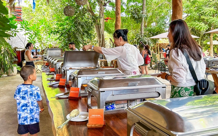 Tourists enjoying buffet during Chichen Itza sunrise tour in lush outdoor setting.