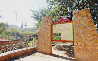 Entrance sign at Ouzoud Waterfalls trailhead, Morocco, with tourist in background.