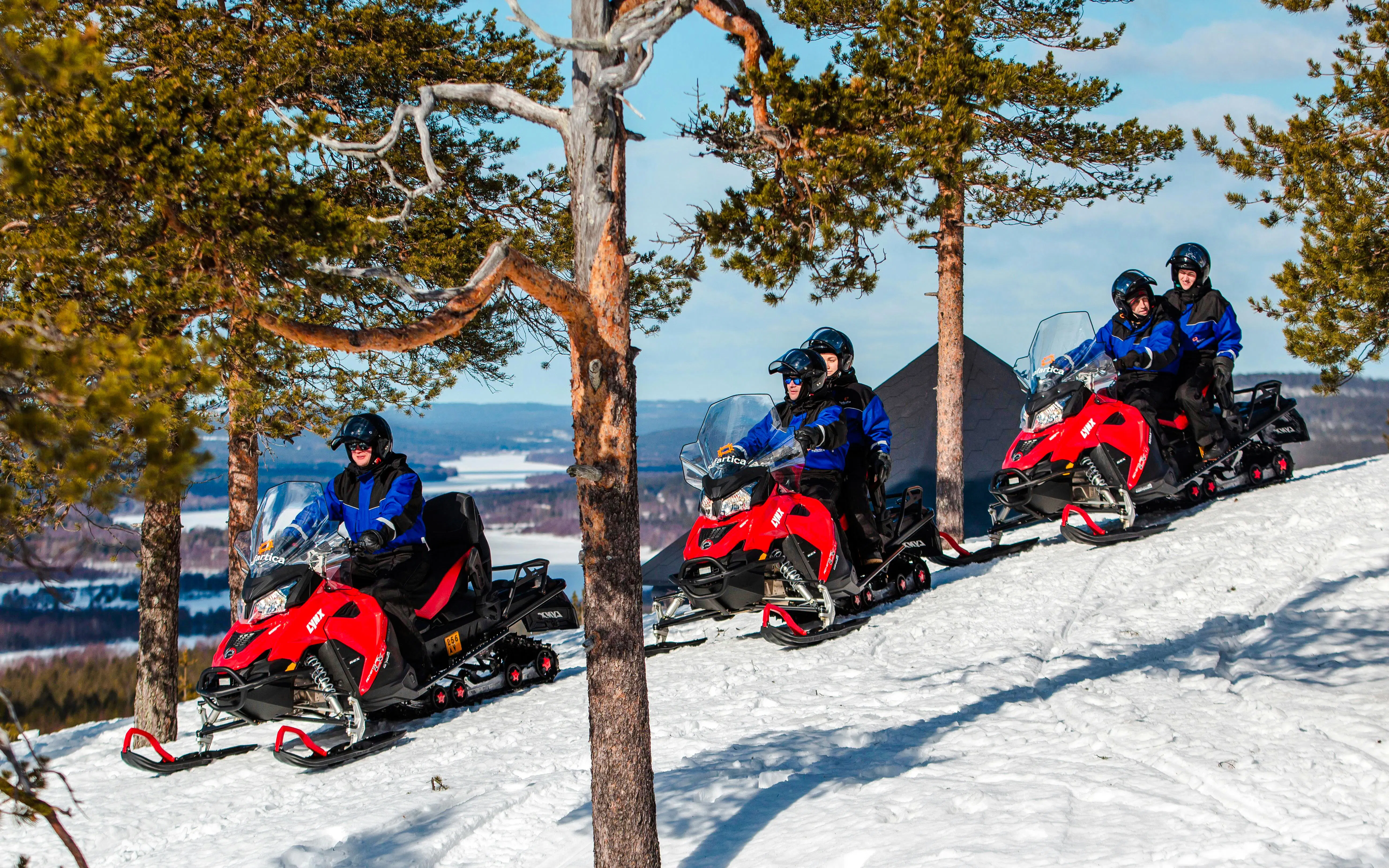 Snowmobilers ride through snowy forest in Lapland.