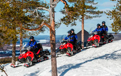 Snowmobilers ride through snowy forest in Lapland.