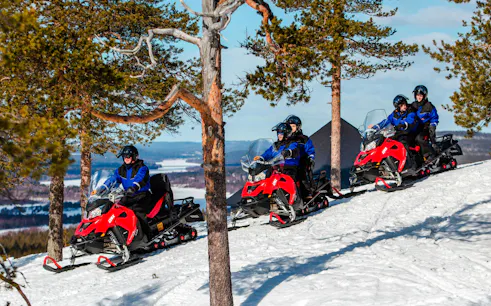 Snowmobilers ride through snowy forest in Lapland.