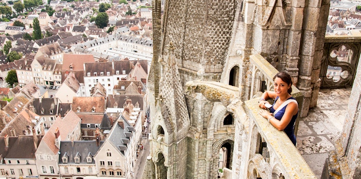 Visitor on Notre Dame balcony overlooking Paris rooftops, using audio guide.