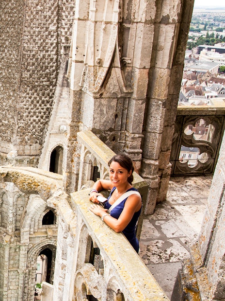 Visitor on Notre Dame balcony overlooking Paris rooftops, using audio guide.