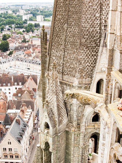 Visitor on Notre Dame balcony overlooking Paris rooftops, using audio guide.