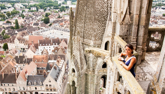 Visitor on Notre Dame balcony overlooking Paris rooftops, using audio guide.