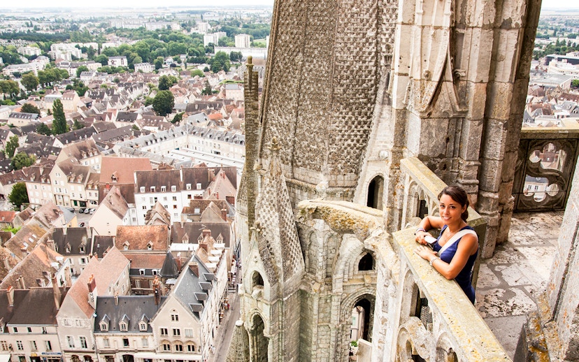 Visitor on Notre Dame balcony overlooking Paris rooftops, using audio guide.