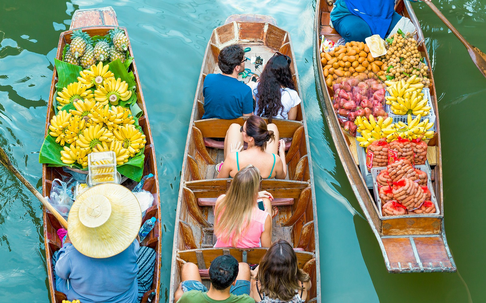 Tourists on a boat navigating Damnoen Saduak Floating Market in Bangkok.
