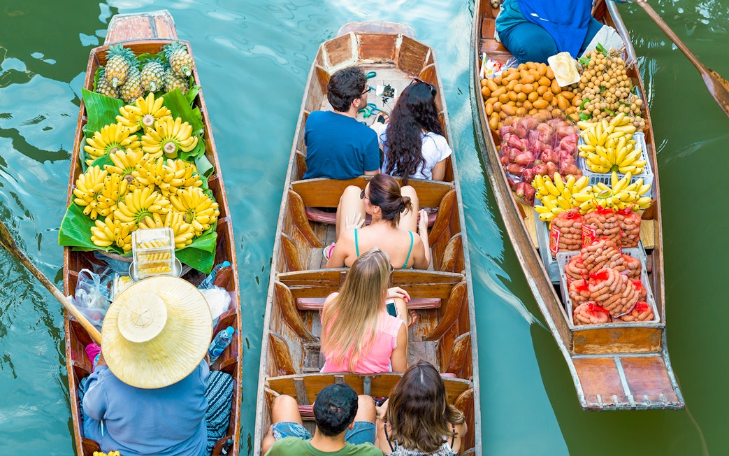 Tourists in a boat at Damnoen Saduak Floating Market surrounded by fruit-laden boats.
