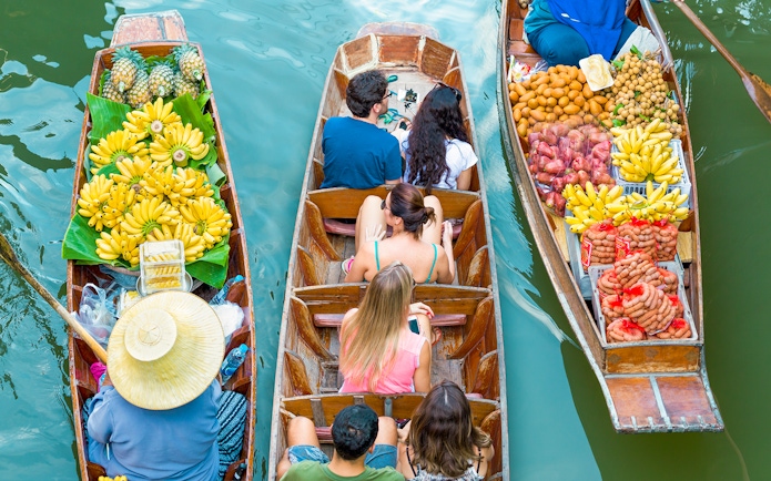 Tourists in a boat at Damnoen Saduak Floating Market surrounded by fruit-laden boats.