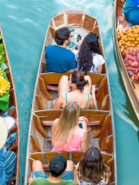Tourists in a boat at Damnoen Saduak Floating Market surrounded by fruit-laden boats.