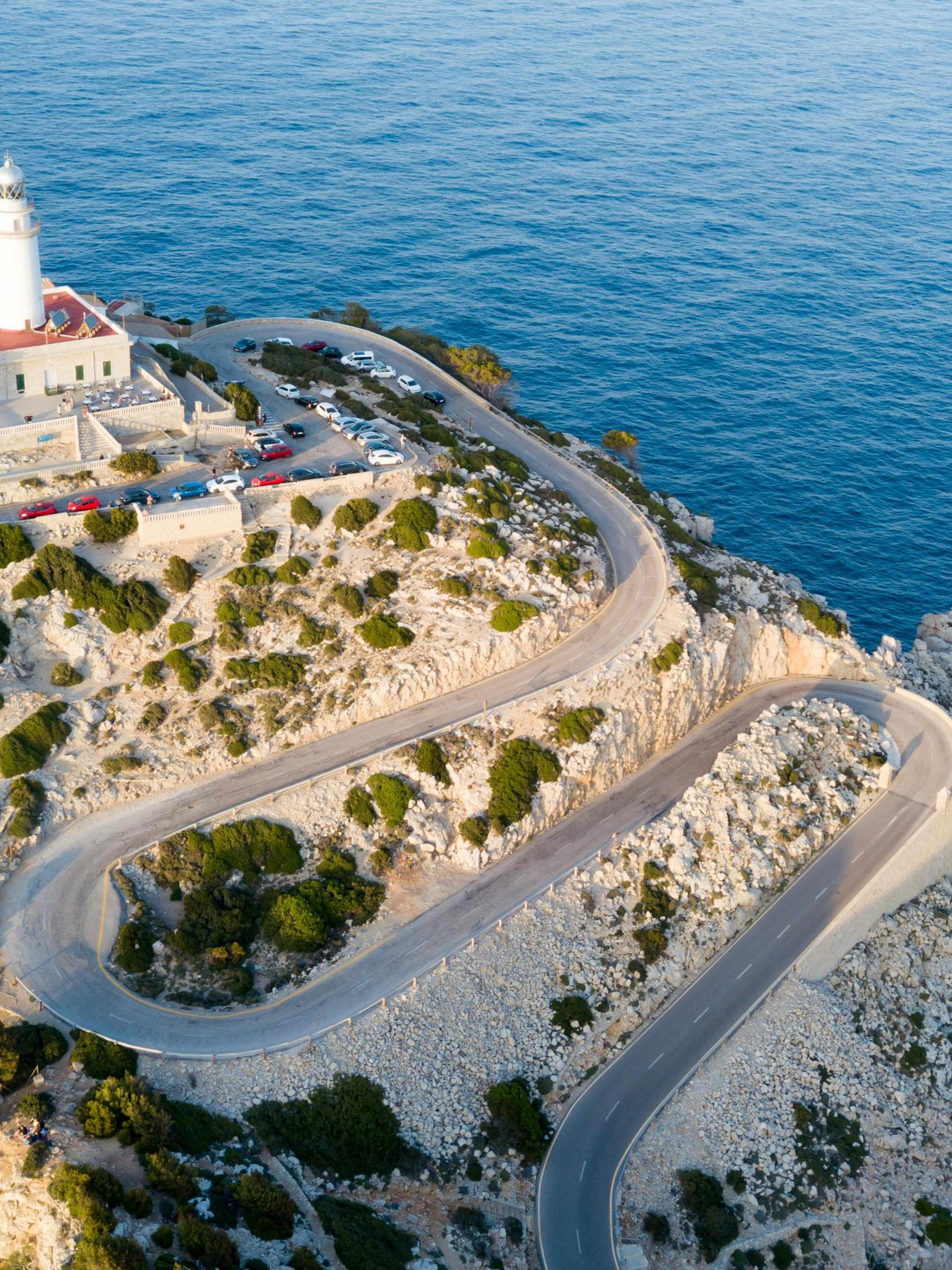 Lighthouse at Cape Formentor, Mallorca, perched on a cliff with winding road and ocean view.
