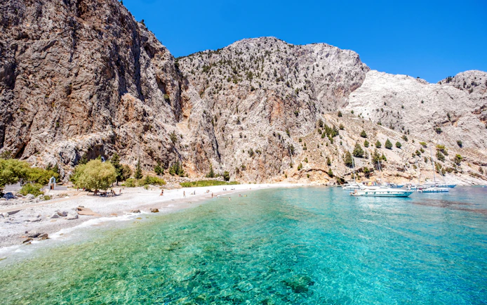 Boats anchored in turquoise waters near rocky cliffs at a beach on Symi Island, Rhodes.