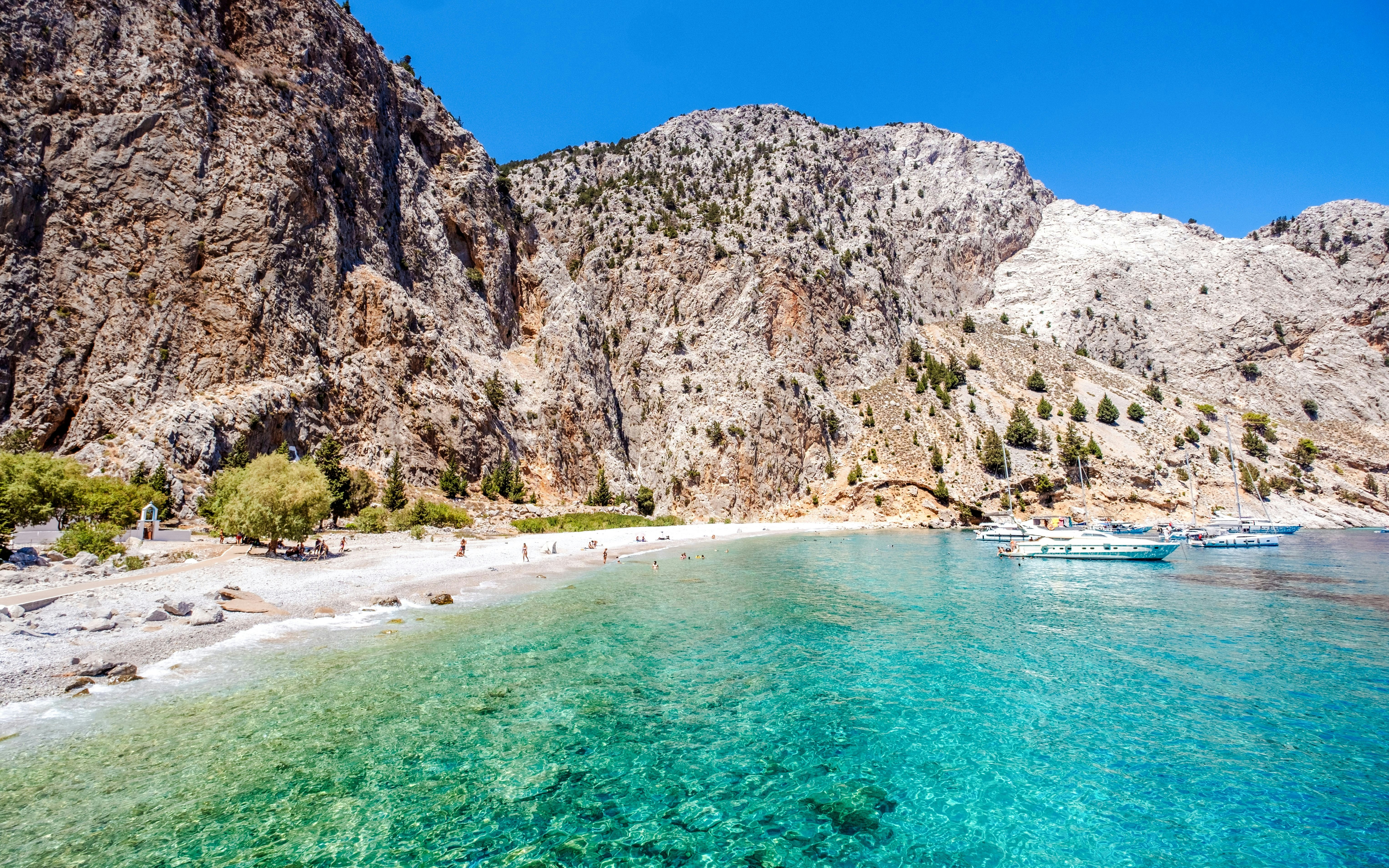 Boats anchored in turquoise waters near rocky cliffs at a beach on Symi Island, Rhodes.