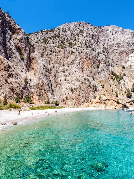 Boats anchored in turquoise waters near rocky cliffs at a beach on Symi Island, Rhodes.