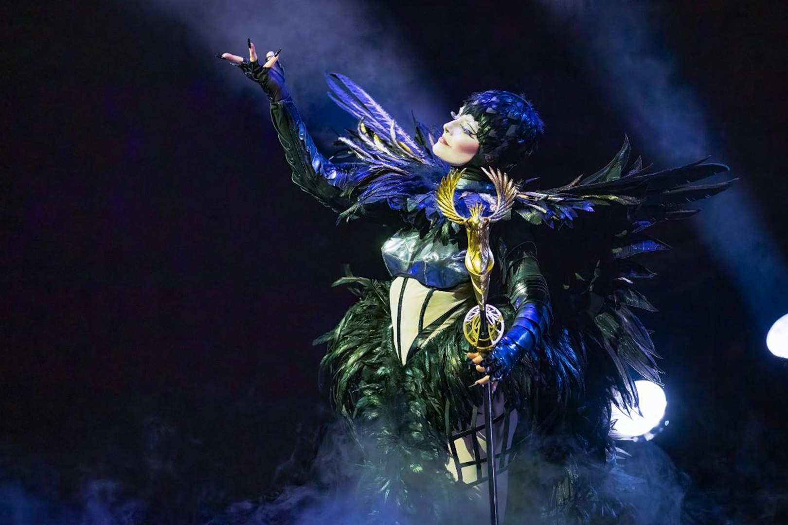 Performer in elaborate costume with feathers and staff during "Awakening" show.