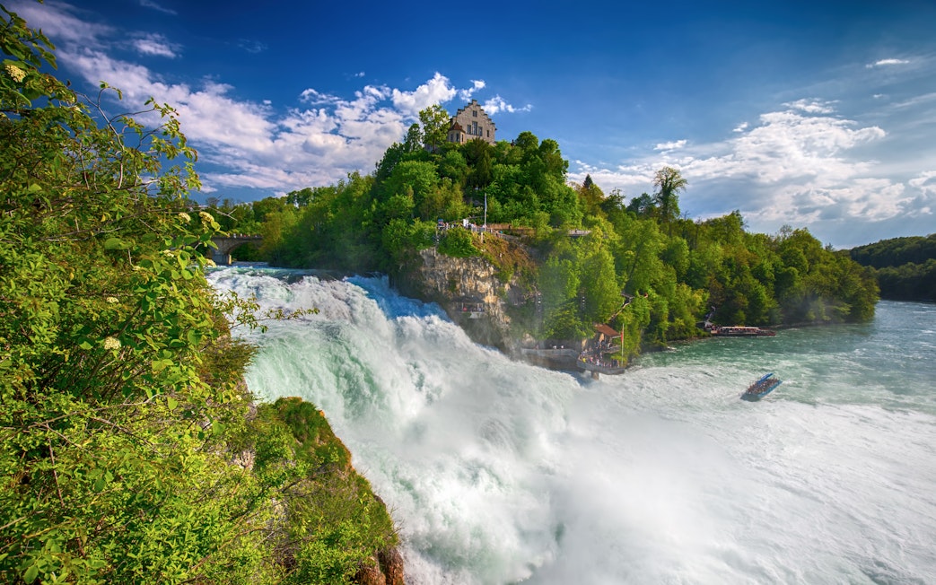Rhine Falls with castle on hill and boat in river, Switzerland.