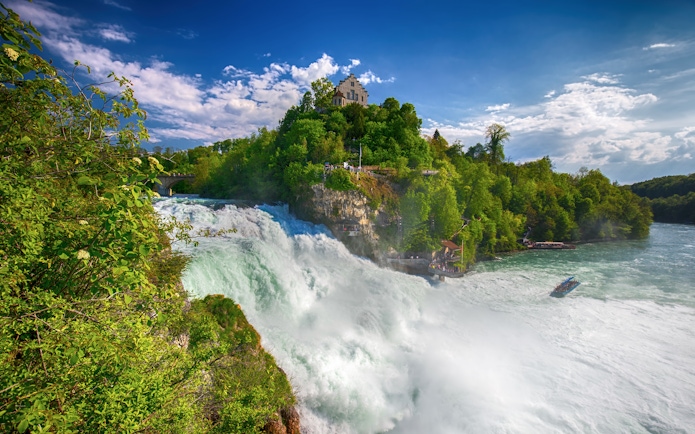 Rhine Falls with castle on hill and boat in river, Switzerland.