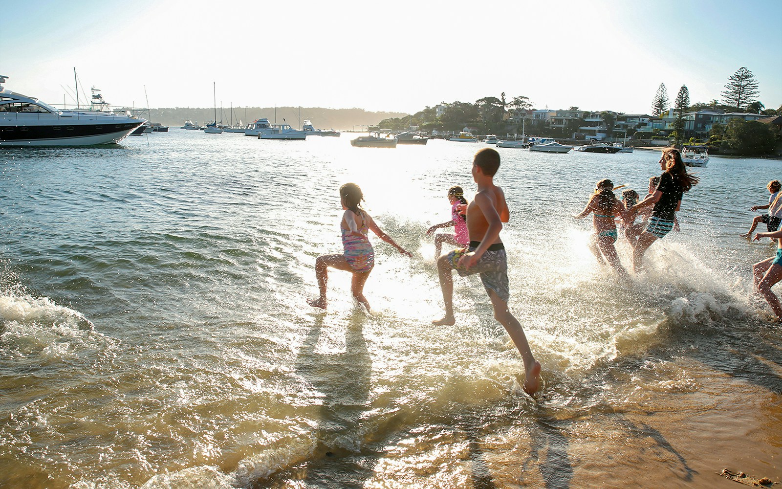 Children playing in the water at Sydney Harbour with boats in the background.