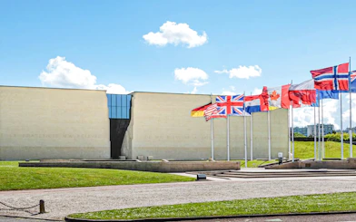 Exteriors of the Caen Memorial Museum with international flags displayed.