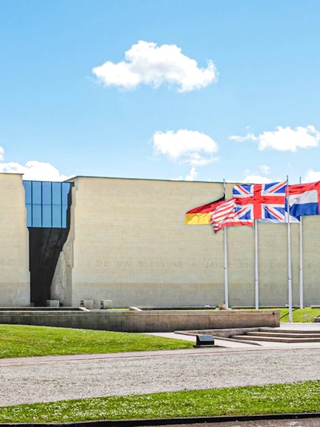 Exteriors of the Caen Memorial Museum with international flags displayed.