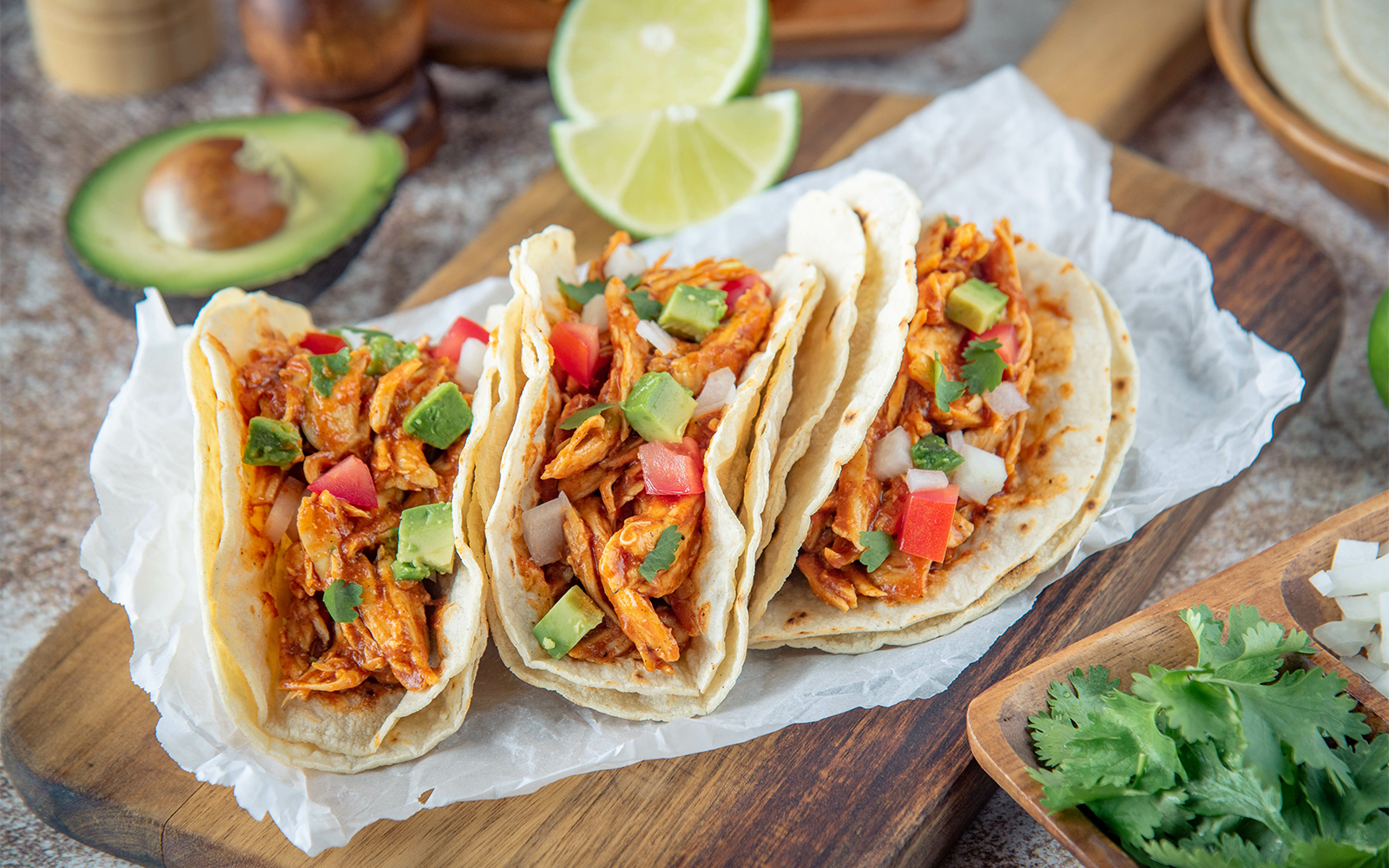 Three chicken tacos with avocado and tomato on a wooden board, Mexican food.