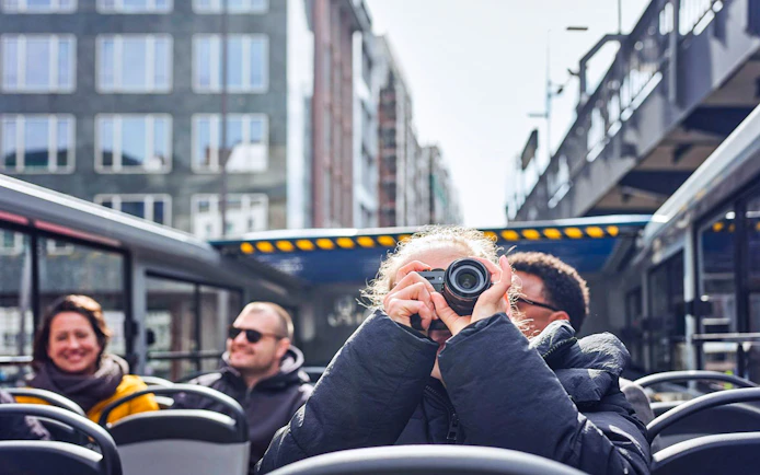 Tourist photographing cityscape on Hamburg Hop-On Hop-Off bus tour.