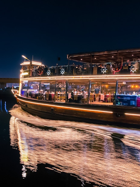 Dubai Canal cruise boat at night with city skyline in background.