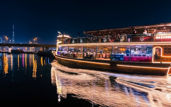 Dubai Canal cruise boat at night with city skyline in background.