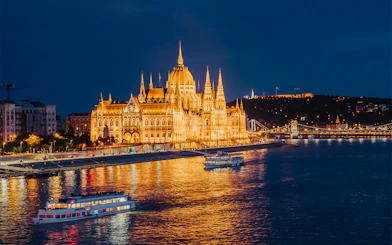 Nighttime cruise on the Danube River by the illuminated Hungarian Parliament in Budapest.