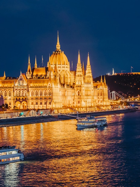 Nighttime cruise on the Danube River by the illuminated Hungarian Parliament in Budapest.