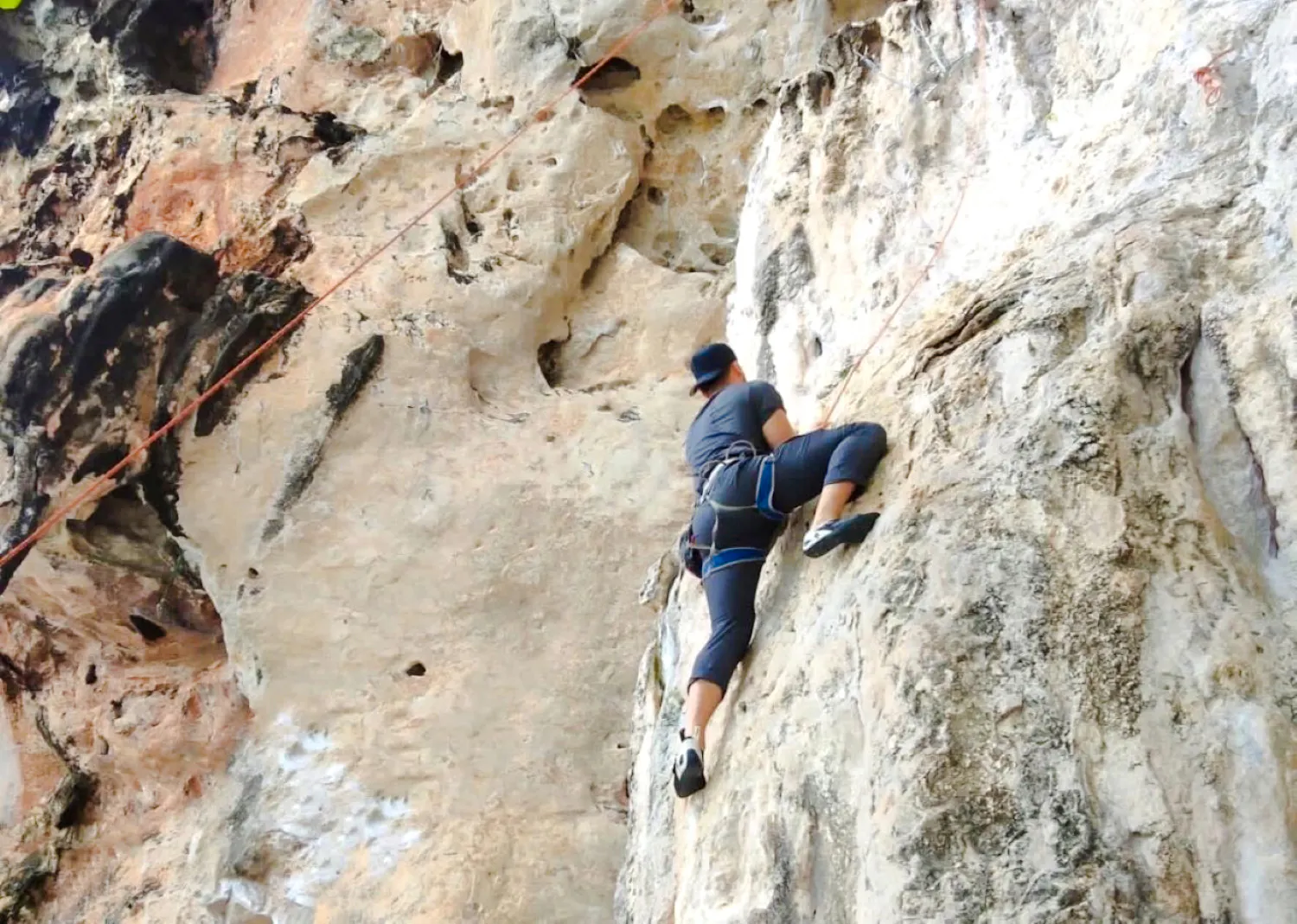 Rock climber scaling limestone cliff at Railay Beach, Krabi.