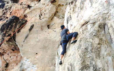 Rock climber scaling limestone cliff at Railay Beach, Krabi.