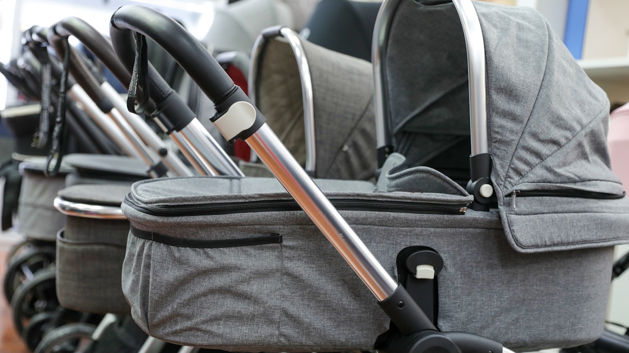 Row of gray baby strollers with adjustable handles in a store display.