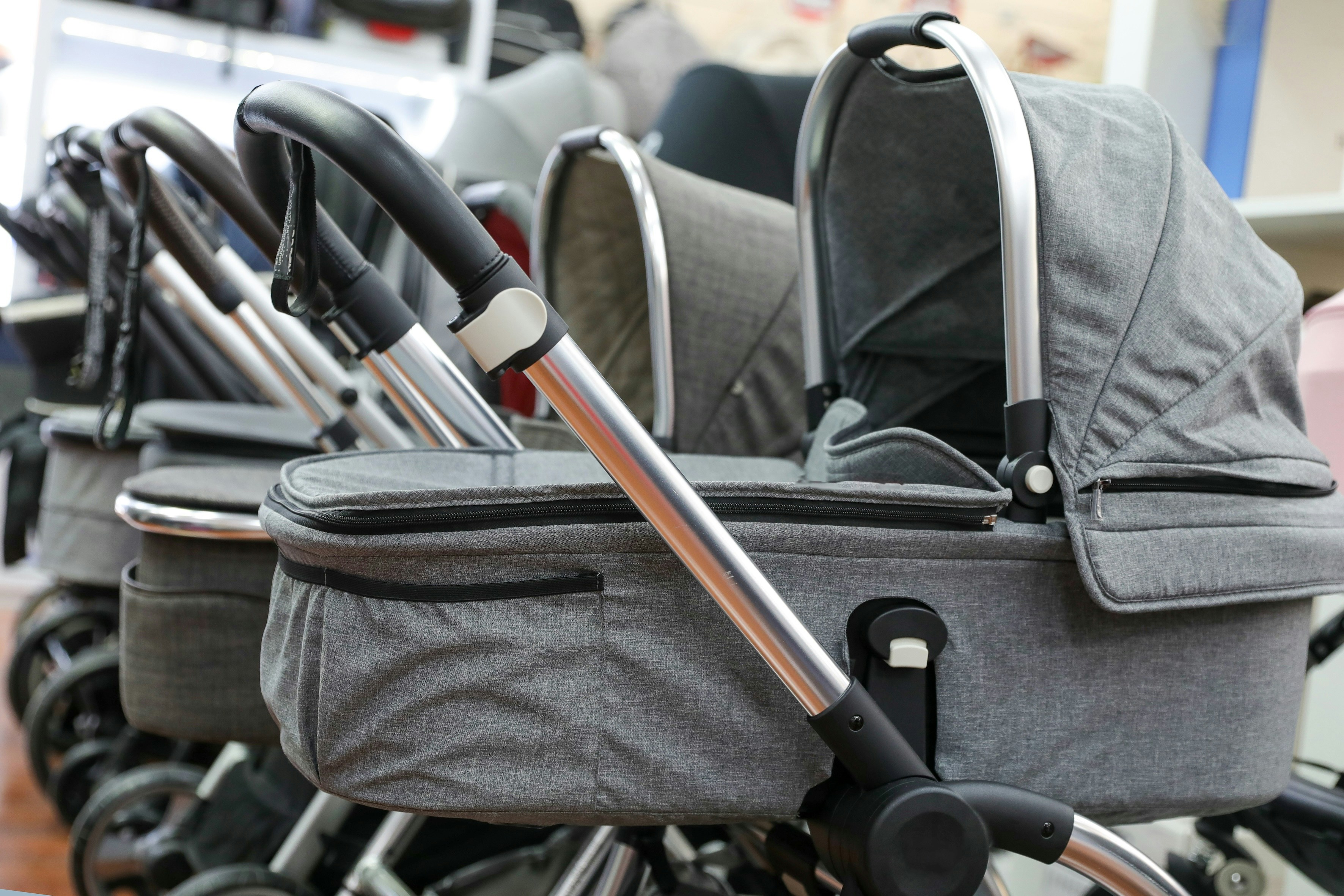 Row of gray baby strollers with adjustable handles in a store display.