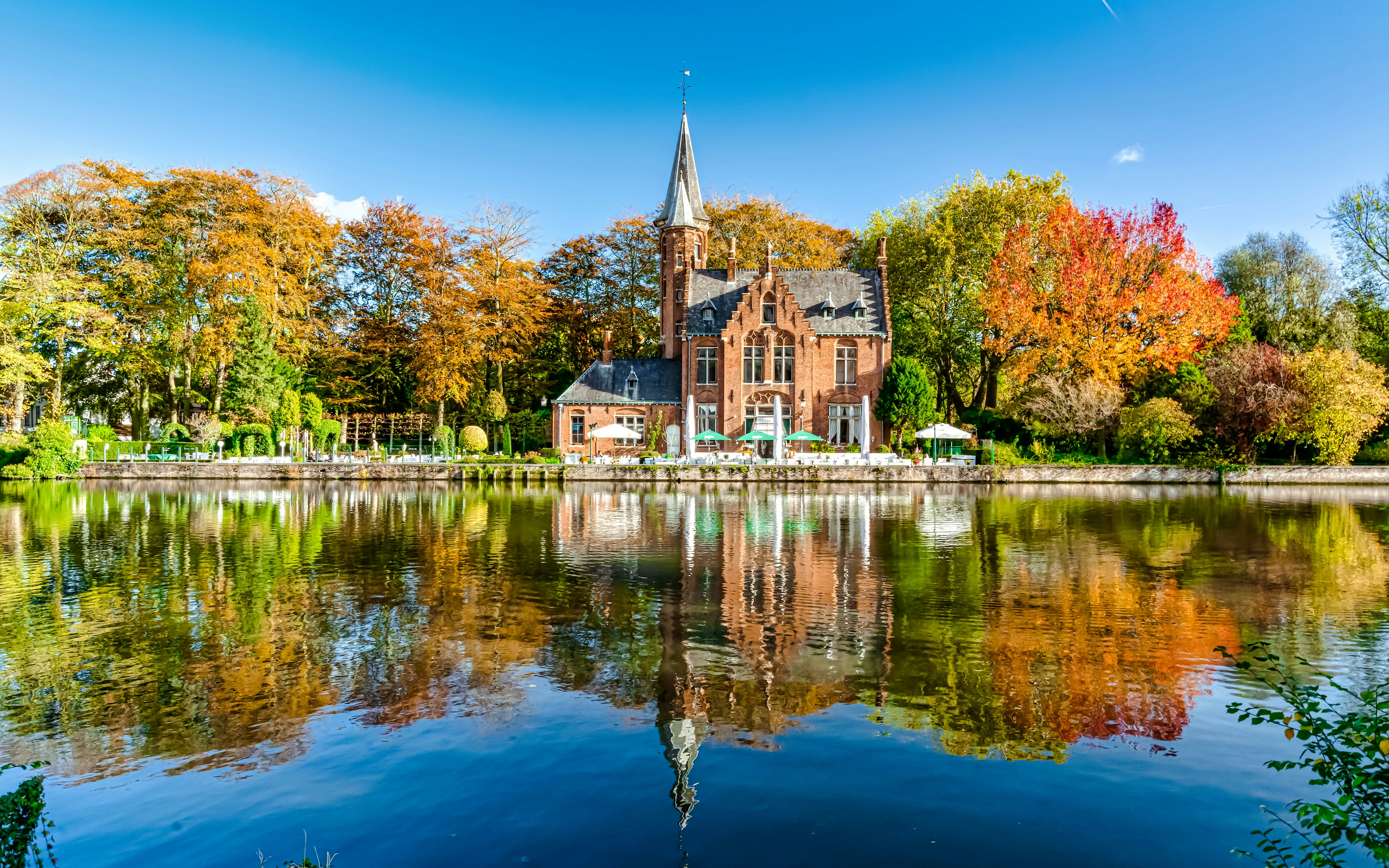 Minnewater Lake and Castle in Bruges, Belgium, reflecting autumn trees.