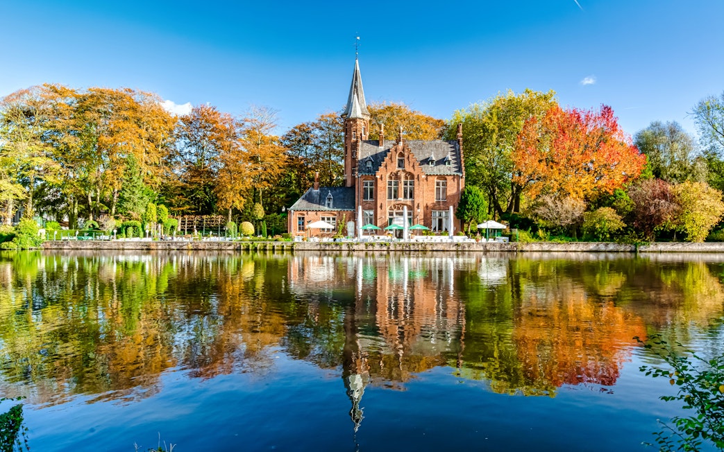 Minnewater Lake and Castle in Bruges, Belgium, reflecting autumn trees.