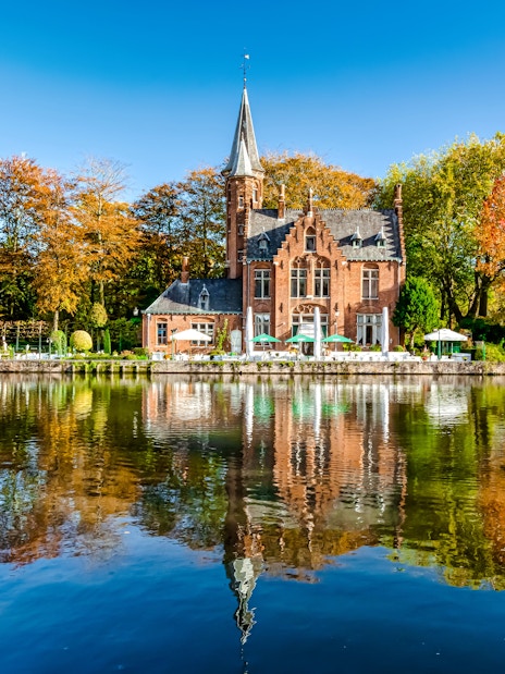 Minnewater Lake and Castle in Bruges, Belgium, reflecting autumn trees.