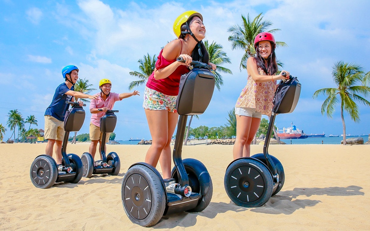 Group enjoying Segway ride on sandy beach with palm trees, part of Gogreen Segway Eco Adventure.