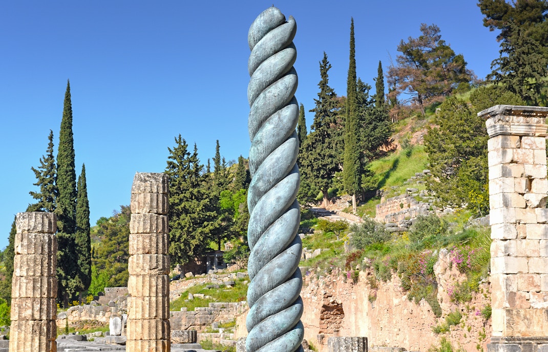 Ancient Serpent Column at Delphi with surrounding ruins and trees.