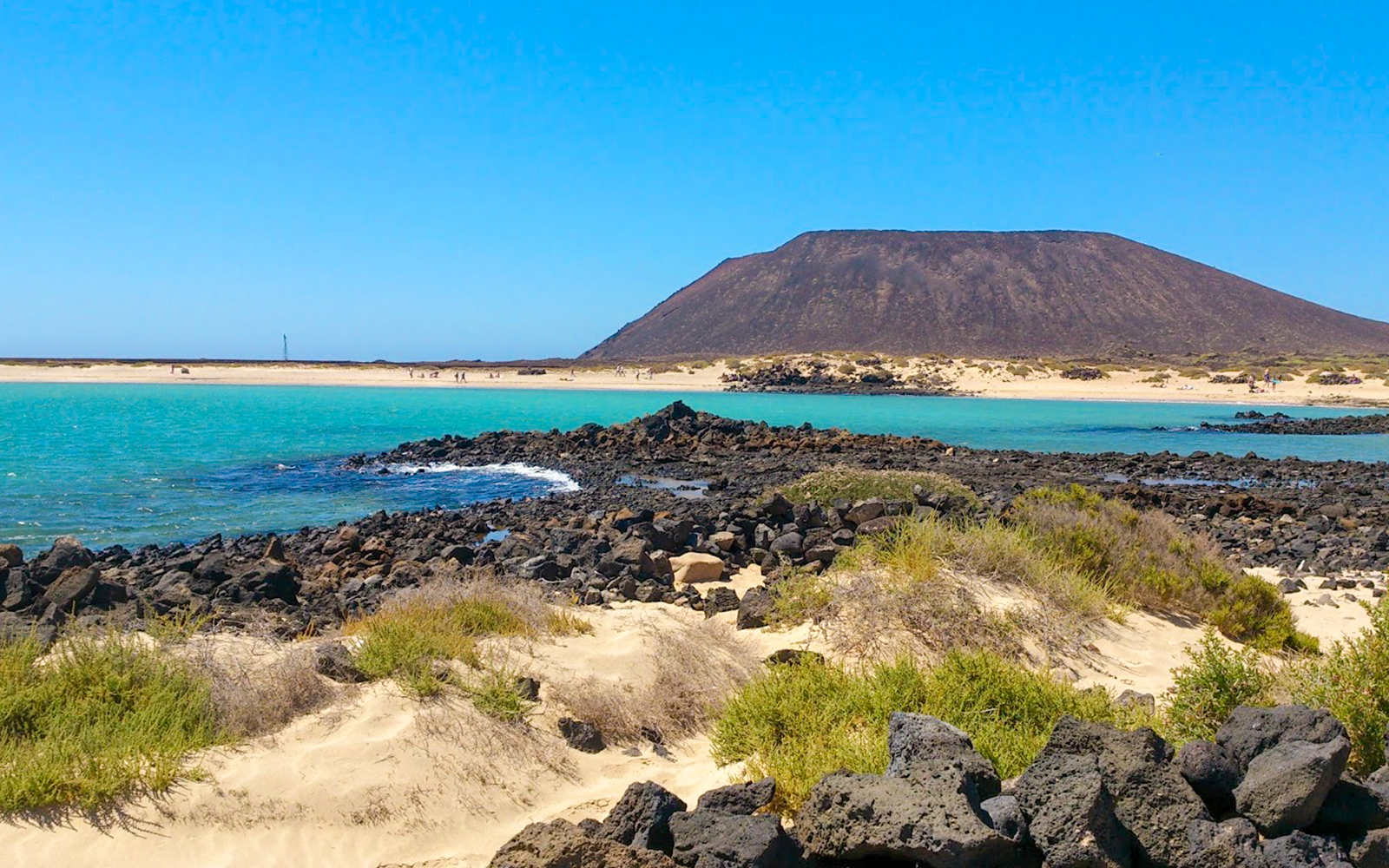 Rocky shoreline and turquoise waters of Lobos Island with volcanic landscape in the background.