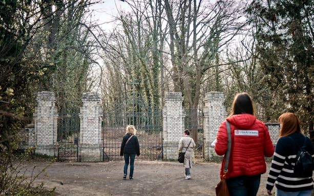 Visitors approaching the entrance of Bohnice Psychiatric Hospital's abandoned cemetery in Prague.